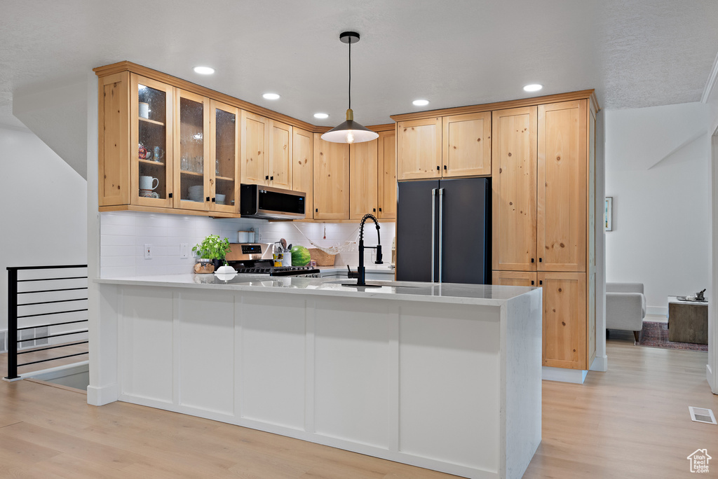 Kitchen with appliances with stainless steel finishes, light brown cabinets, light wood-style flooring, a peninsula, and glass insert cabinets