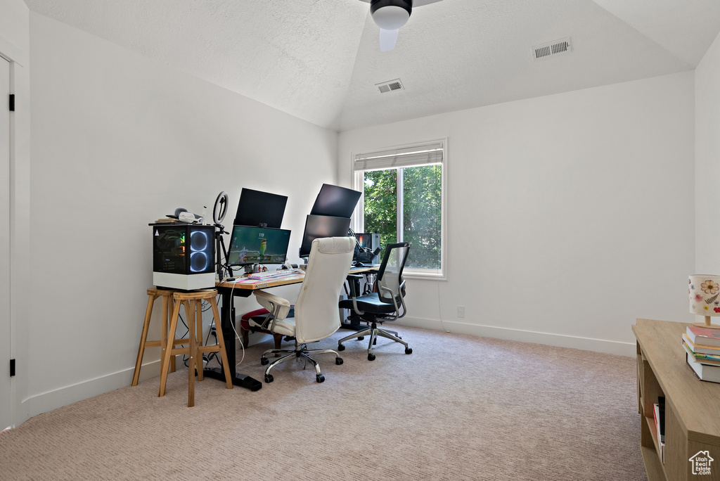 Carpeted home office featuring lofted ceiling, ceiling fan, and a textured ceiling