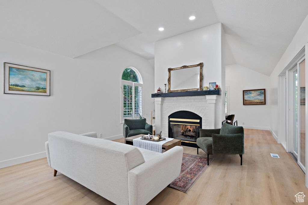 Living room with a brick fireplace, light wood-type flooring, lofted ceiling, and recessed lighting