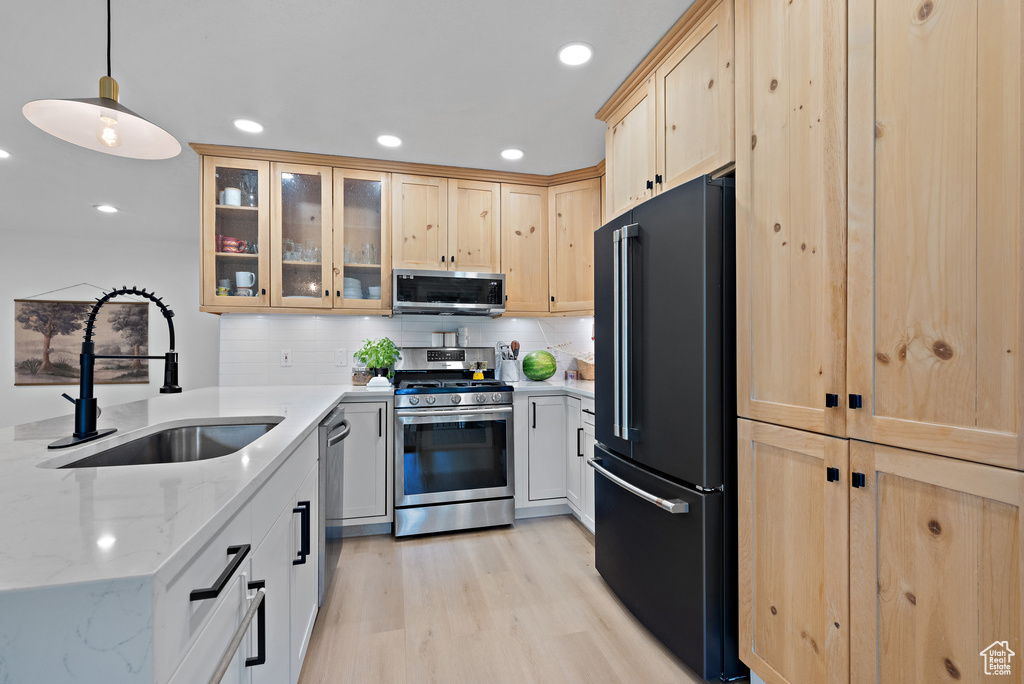 Kitchen featuring stainless steel appliances, light brown cabinetry, a peninsula, light stone countertops, and glass insert cabinets