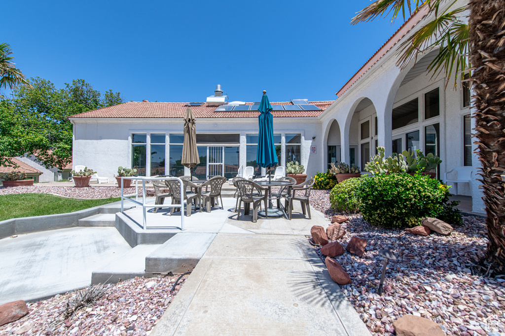 Rear view of property featuring stucco siding, a tile roof, a patio, and roof mounted solar panels