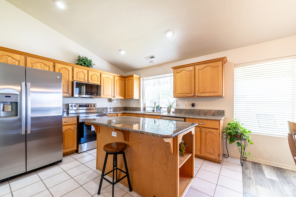 Kitchen featuring appliances with stainless steel finishes, a kitchen island, lofted ceiling, a breakfast bar area, and a textured ceiling