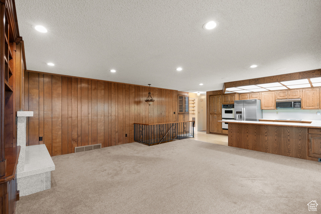 Unfurnished living room featuring light carpet, wood walls, recessed lighting, and a textured ceiling