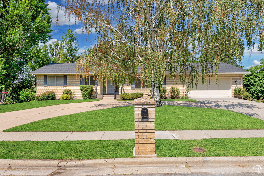 View of front of home with driveway, brick siding, a front lawn, and a garage