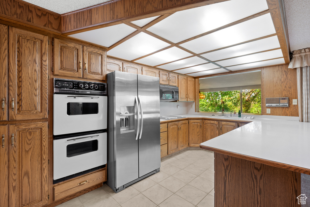 Kitchen with black appliances, light countertops, light tile patterned floors, and brown cabinets