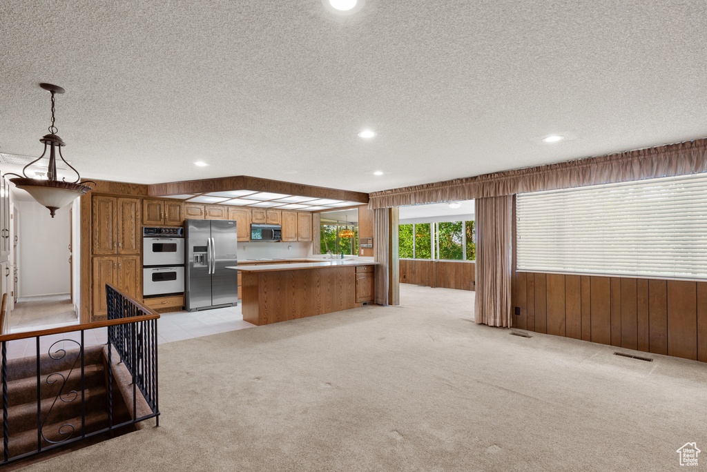 Kitchen featuring stainless steel refrigerator with ice dispenser, a textured ceiling, light colored carpet, white double oven, and wood walls