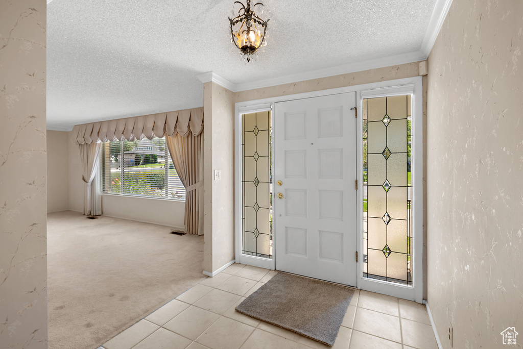 Carpeted entryway with a textured ceiling, ornamental molding, tile patterned floors, and a chandelier