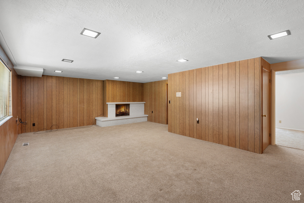 Unfurnished living room with a lit fireplace, wood walls, carpet, a textured ceiling, and recessed lighting