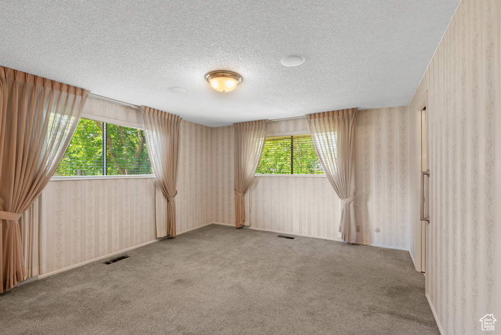 Carpeted spare room with wallpapered walls and a textured ceiling