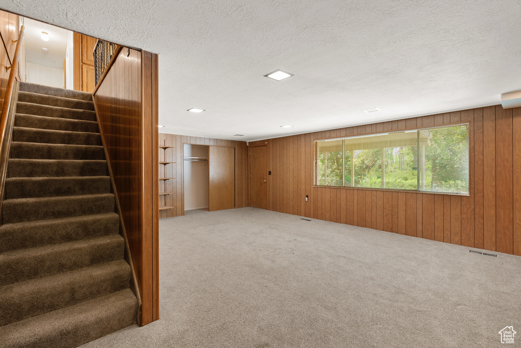 Basement with carpet floors, stairs, wood walls, and a textured ceiling