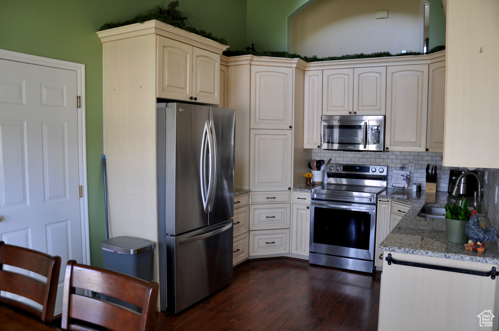 Kitchen featuring stainless steel appliances, dark wood-style flooring, decorative backsplash, light stone counters, and cream cabinets