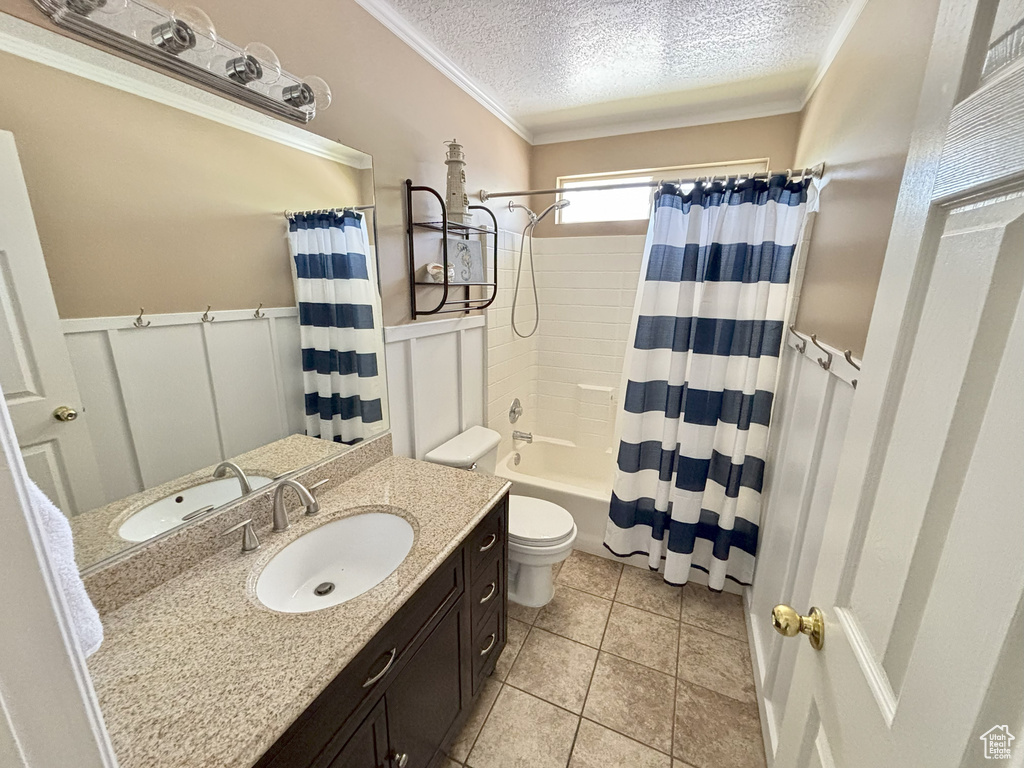 Bathroom with a textured ceiling, vanity, shower / tub combo with curtain, ornamental molding, and a wainscoted wall