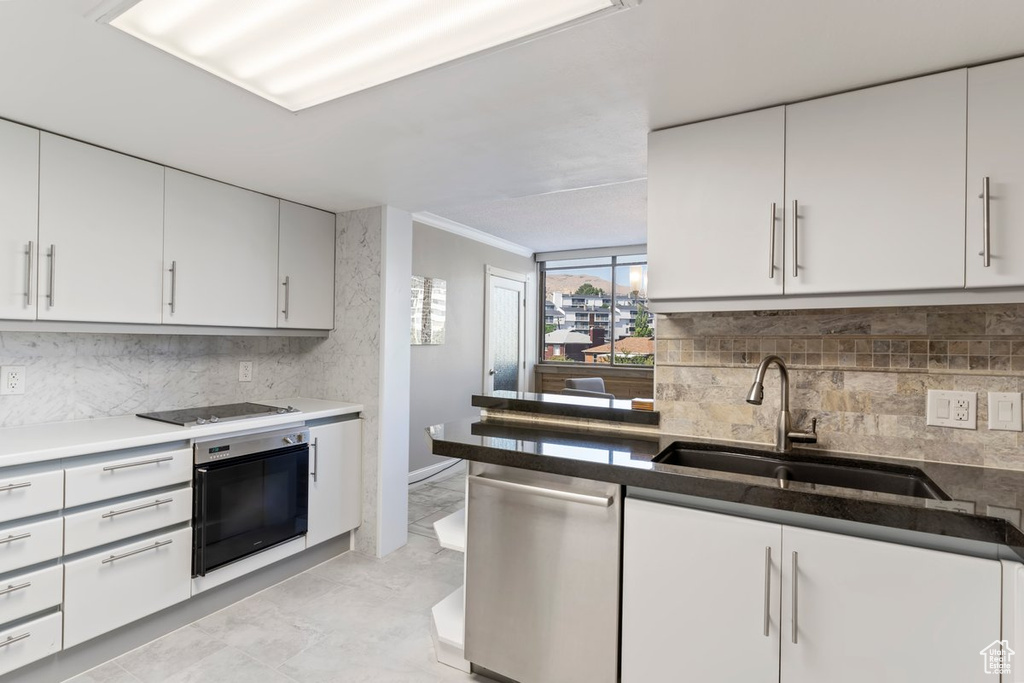 Kitchen with appliances with stainless steel finishes, decorative backsplash, light marble finish floors, ornamental molding, and white cabinetry