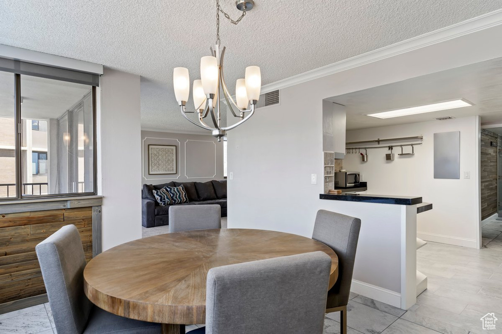 Dining space featuring a chandelier, crown molding, and a textured ceiling