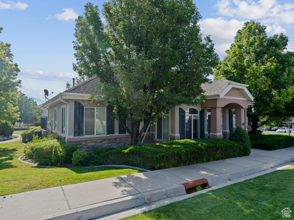 Obstructed view of property featuring a front lawn, stucco siding, stone siding, and roof with shingles