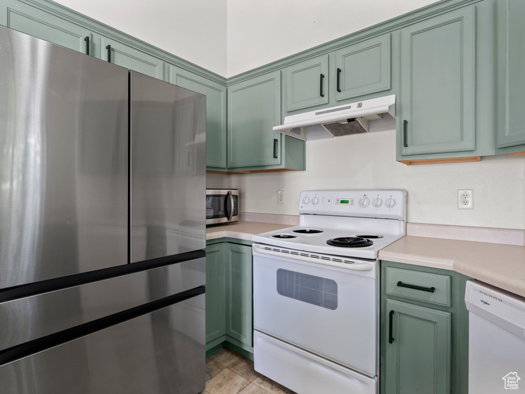 Kitchen featuring stainless steel appliances, green cabinetry, under cabinet range hood, and light countertops