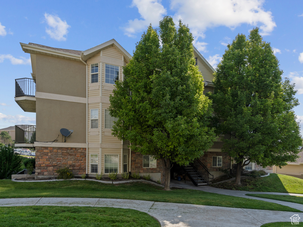 View of front facade with a balcony, stone siding, stairway, a front yard, and stucco siding