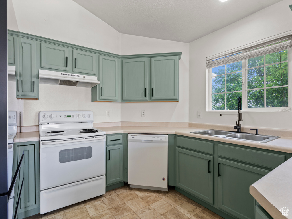 Kitchen with white appliances, green cabinets, under cabinet range hood, lofted ceiling, and light countertops