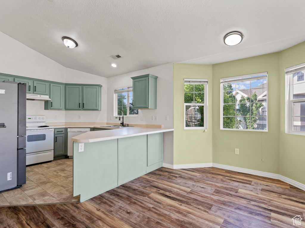 Kitchen featuring white appliances, green cabinets, a peninsula, under cabinet range hood, and healthy amount of natural light