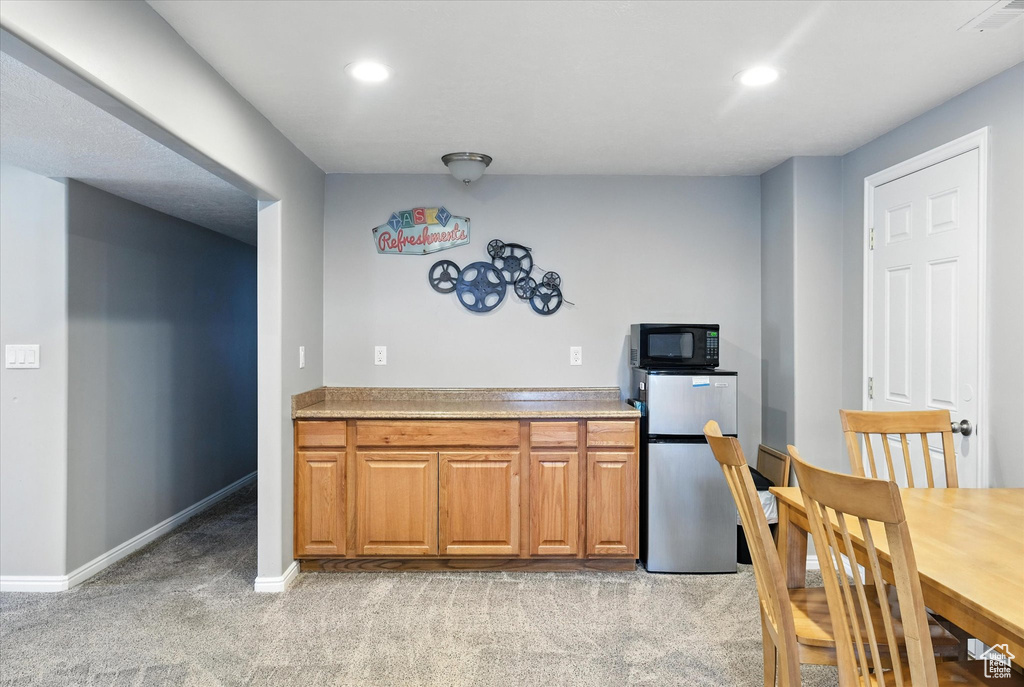 Kitchen with freestanding refrigerator, light carpet, recessed lighting, brown cabinetry, and black microwave