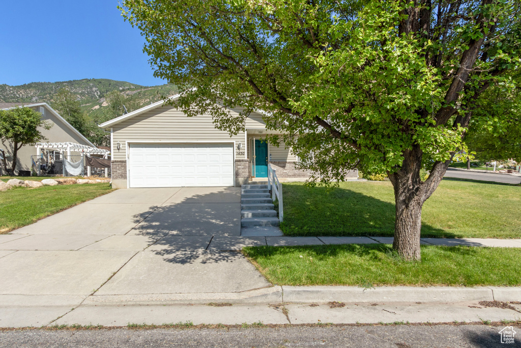View of front of home featuring a front yard, concrete driveway, a mountain view, an attached garage, and brick siding