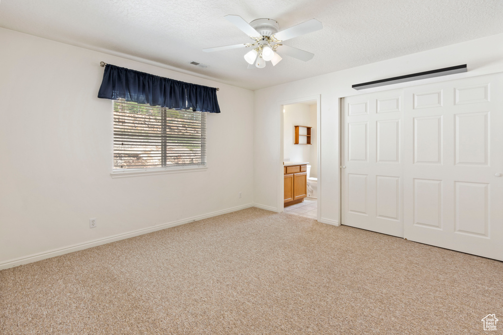Unfurnished bedroom with light colored carpet, ensuite bathroom, a closet, ceiling fan, and a textured ceiling