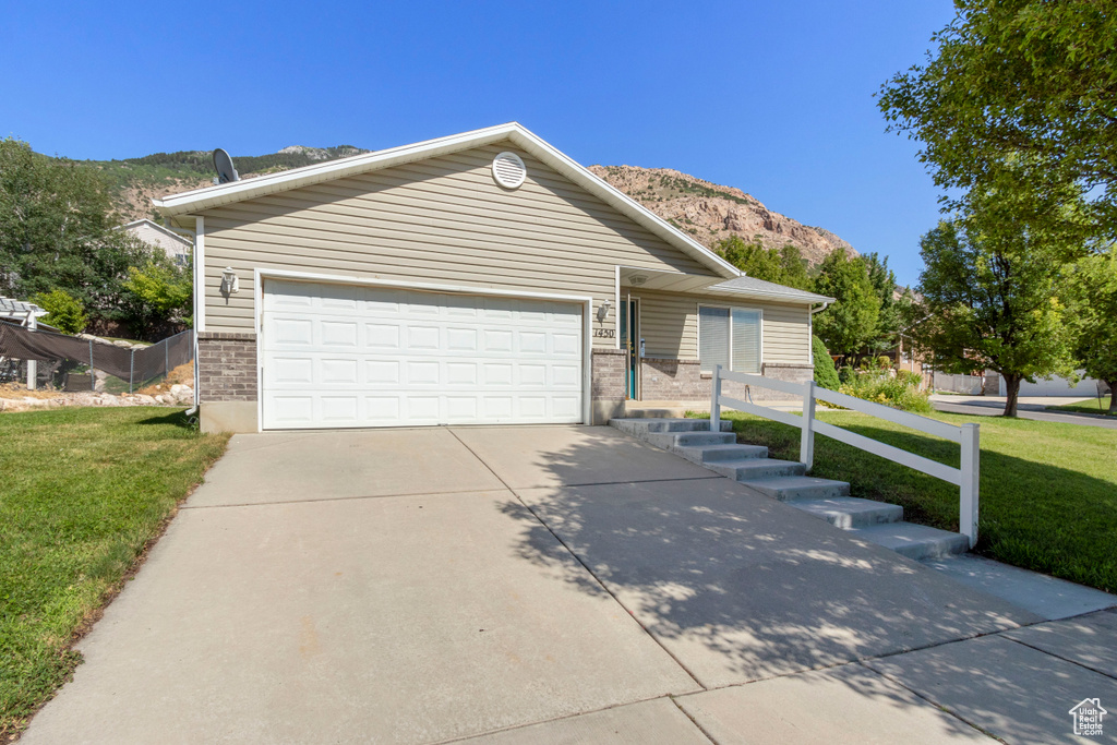 Ranch-style home featuring a mountain view, a front yard, a garage, driveway, and brick siding