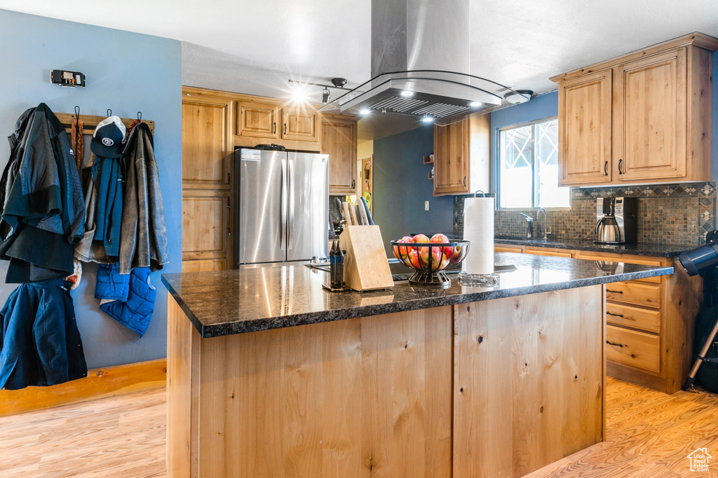 Kitchen with freestanding refrigerator, island range hood, light wood-style floors, a center island, and backsplash