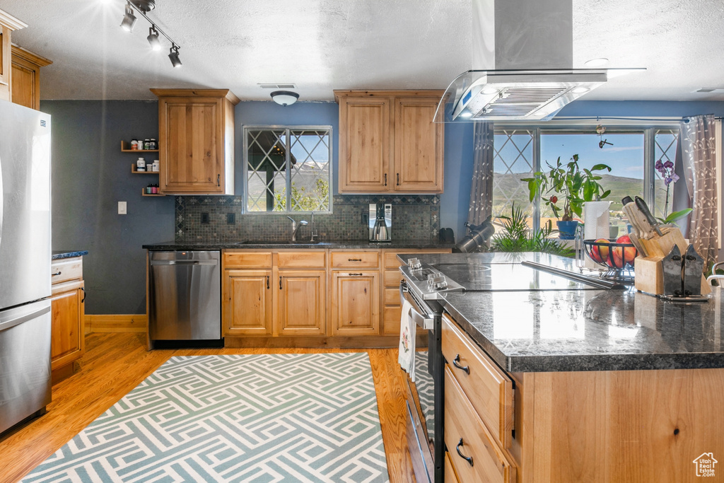 Kitchen featuring stainless steel appliances, island range hood, light wood finished floors, a textured ceiling, and decorative backsplash