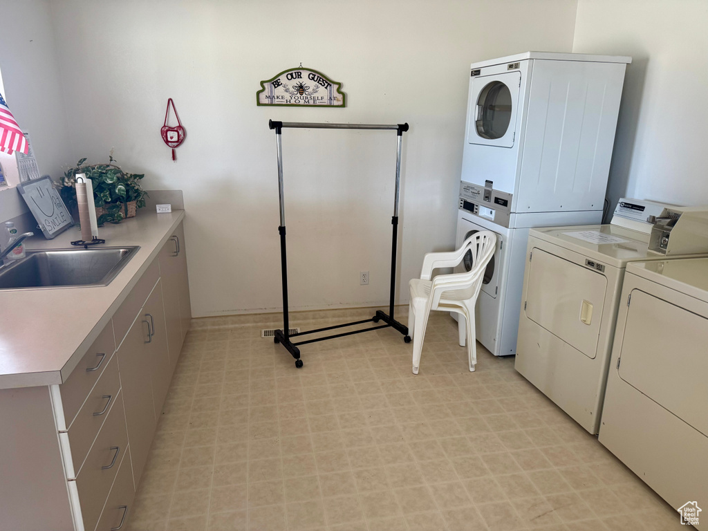 Washroom with stacked washer / drying machine, cabinet space, and light flooring