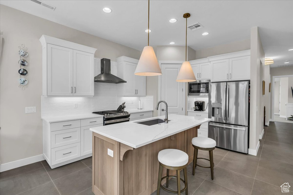 Kitchen with appliances with stainless steel finishes, wall chimney range hood, decorative backsplash, dark tile patterned floors, and white cabinets