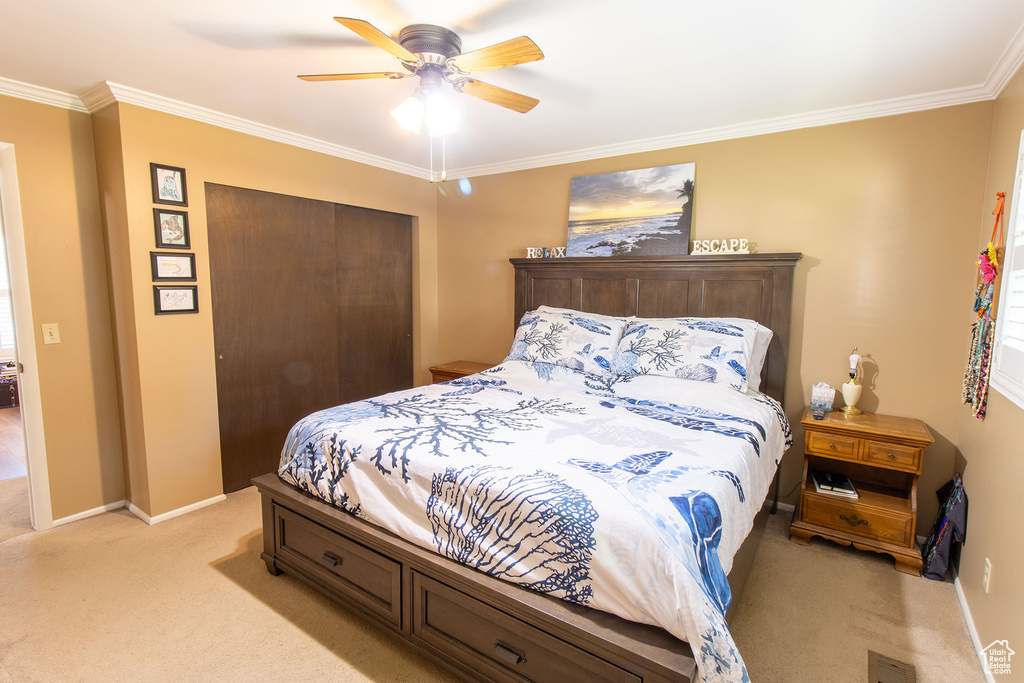 Bedroom with light colored carpet, crown molding, a closet, and ceiling fan
