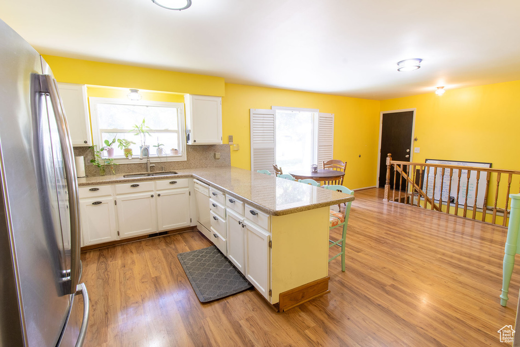 Kitchen featuring freestanding refrigerator, tasteful backsplash, light wood-style floors, white cabinetry, and a peninsula