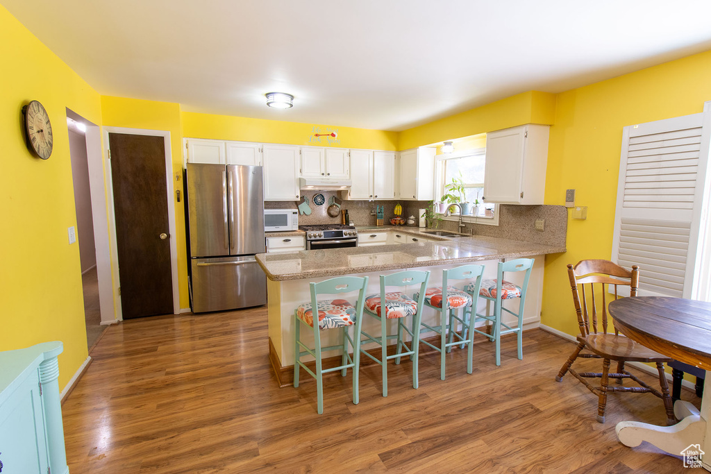 Kitchen featuring stainless steel appliances, a peninsula, wood finished floors, and white cabinets
