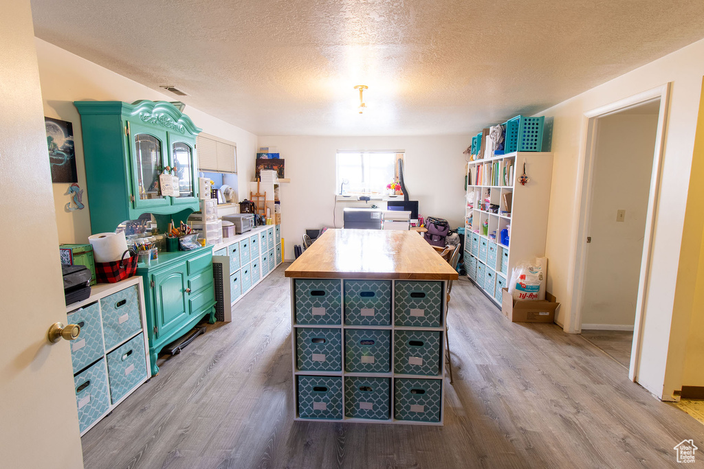 Kitchen featuring butcher block counters, light wood-style floors, a textured ceiling, and a kitchen island