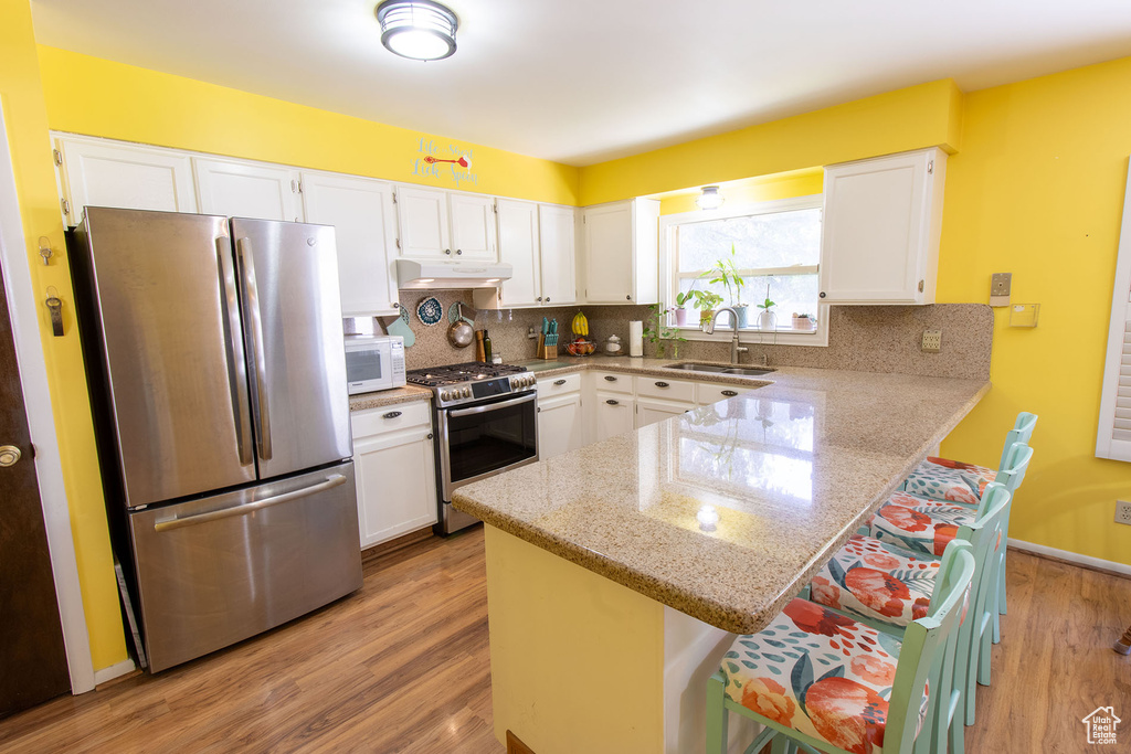 Kitchen with stainless steel appliances, under cabinet range hood, a peninsula, and white cabinets