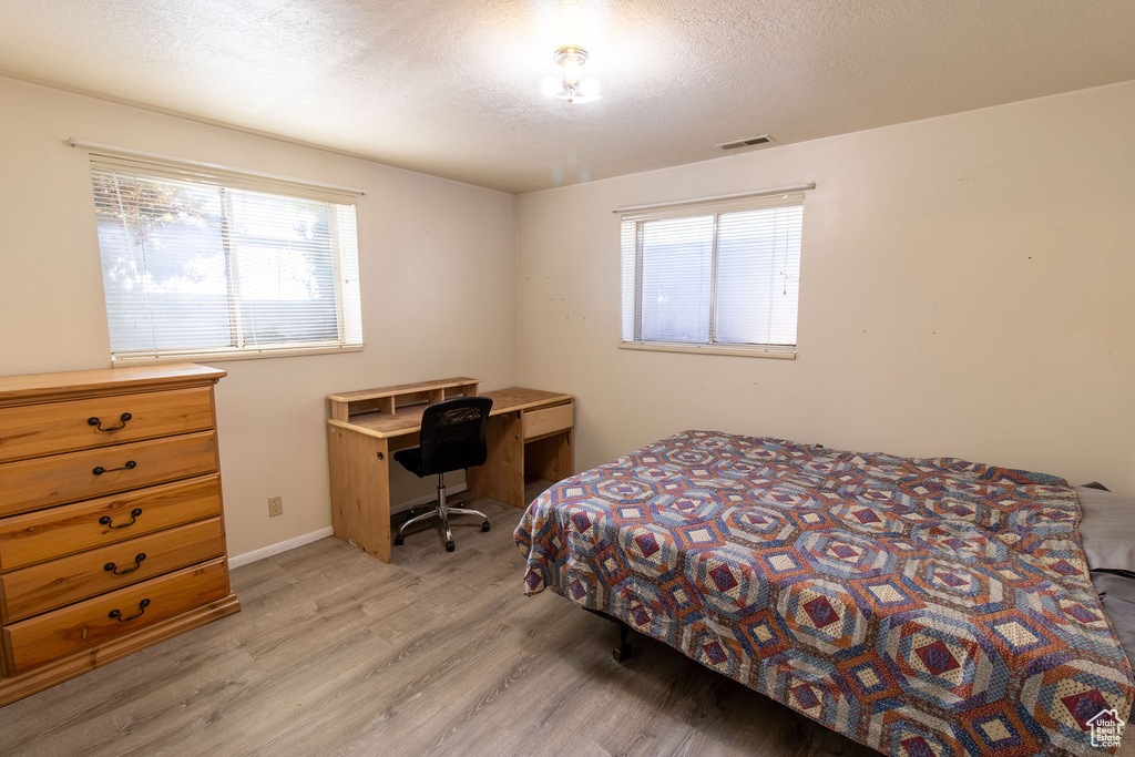 Bedroom with light wood-type flooring, multiple windows, a textured ceiling, and an office area