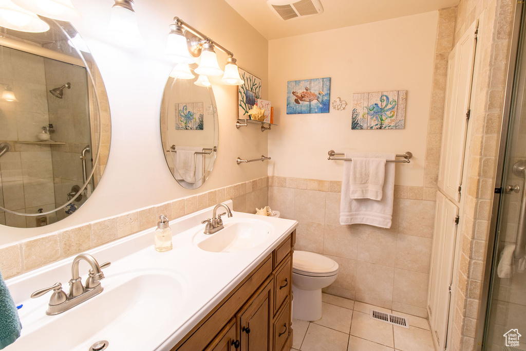 Full bath featuring double vanity, a shower stall, tile patterned floors, wainscoting, and tile walls