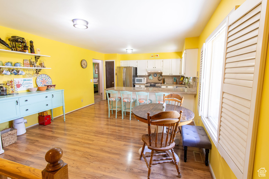 Kitchen featuring stainless steel appliances, a peninsula, white cabinetry, a breakfast bar, and light wood-type flooring