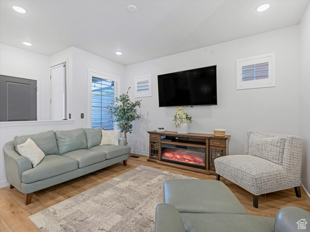 Living room with wood finished floors, recessed lighting, and a glass covered fireplace
