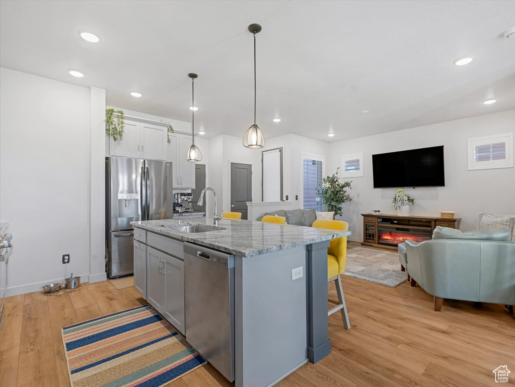 Kitchen with appliances with stainless steel finishes, a breakfast bar, light wood-style floors, open floor plan, and recessed lighting