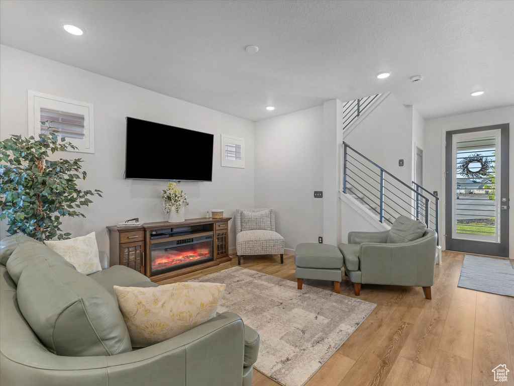Living room with stairs, light wood finished floors, a glass covered fireplace, and recessed lighting