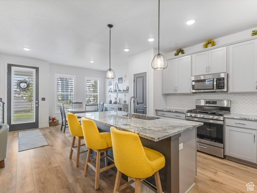 Kitchen featuring appliances with stainless steel finishes, decorative backsplash, a kitchen island with sink, light stone counters, and recessed lighting