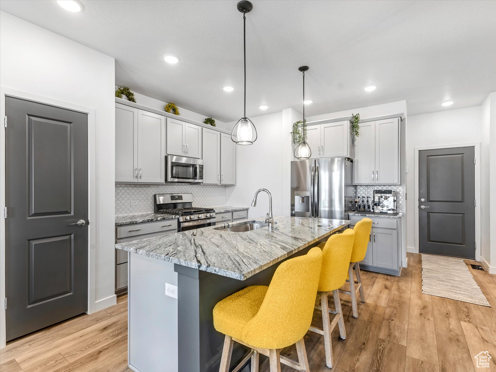 Kitchen featuring stainless steel appliances, tasteful backsplash, a breakfast bar, light stone counters, and light wood-style flooring
