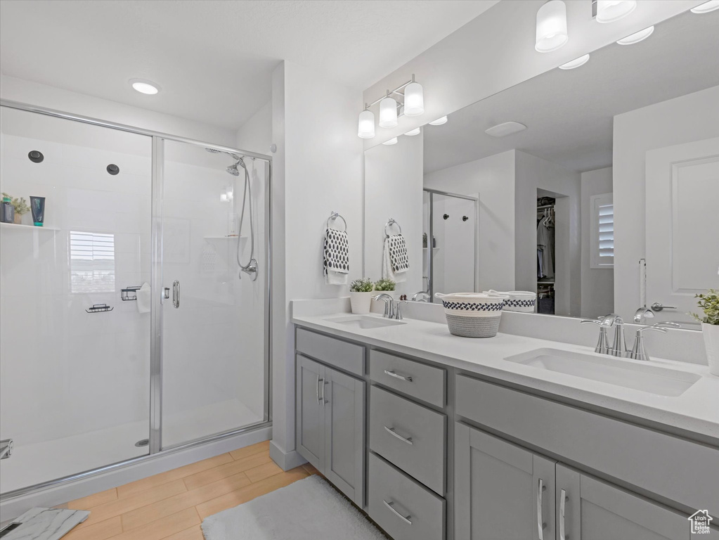 Bathroom featuring a shower stall, double vanity, and wood finished floors