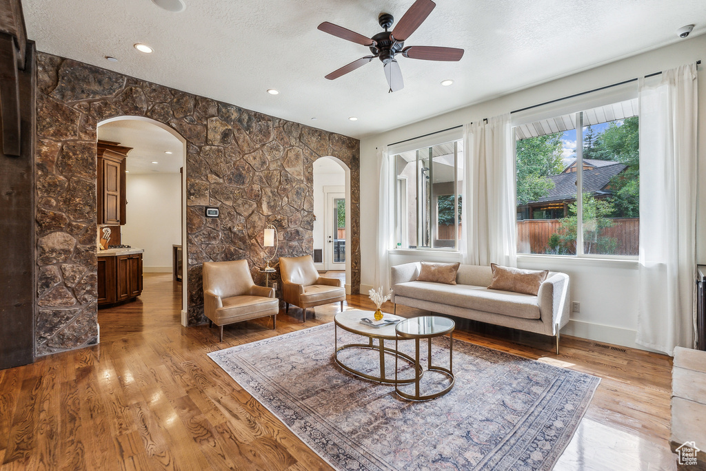Living area with arched walkways, a ceiling fan, light wood-style floors, and recessed lighting