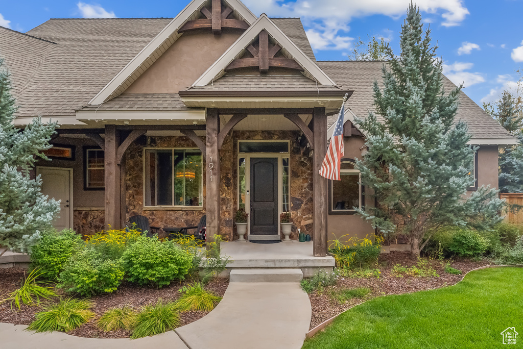 Doorway to property with a shingled roof, a porch, and stone siding