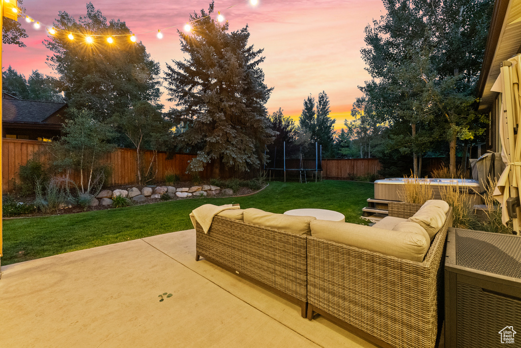 Patio terrace at dusk featuring a trampoline, a patio, a fenced backyard, and an outdoor living space
