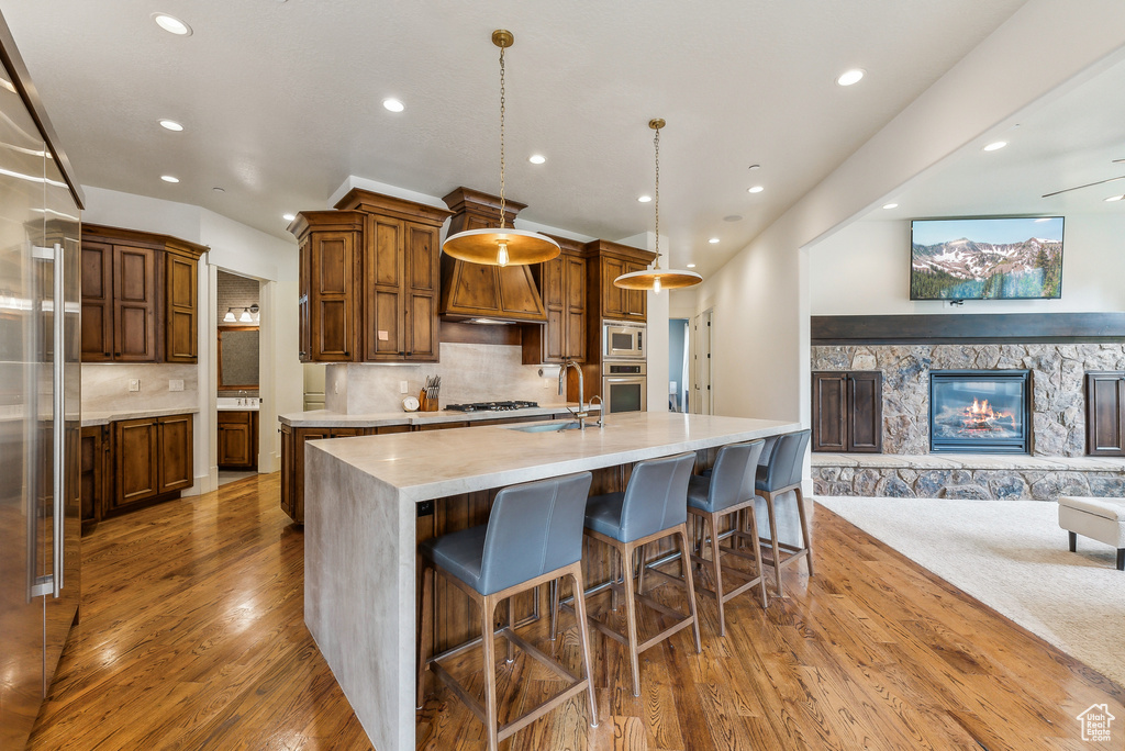 Kitchen featuring a large island with sink, built in appliances, wood finished floors, open floor plan, and recessed lighting