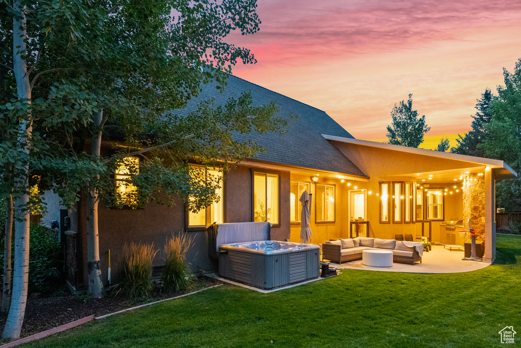 Back of property at dusk with an outdoor living space, a patio, a lawn, a hot tub, and a shingled roof